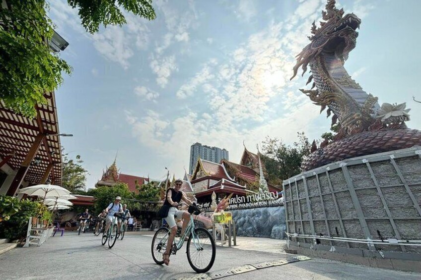 A street with a dragon sculpture, bicycles, and traditional Thai architecture. 1
