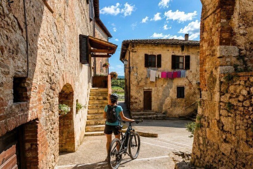 A narrow street with stone buildings, a cyclist, and laundry hanging outside. 3