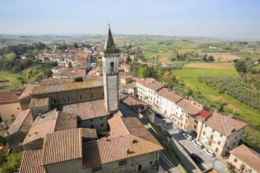 A town with a prominent tower, terracotta-roofed buildings, and a hilly landscape in the background. 3