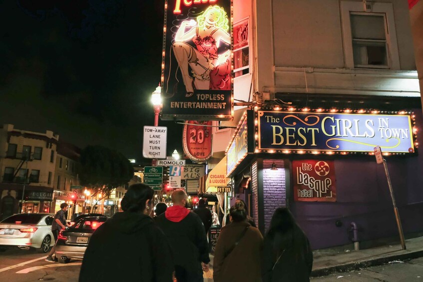 A busy street at night with illuminated signs for 'Topless Entertainment' and 'The Best Girls in Town.' 5