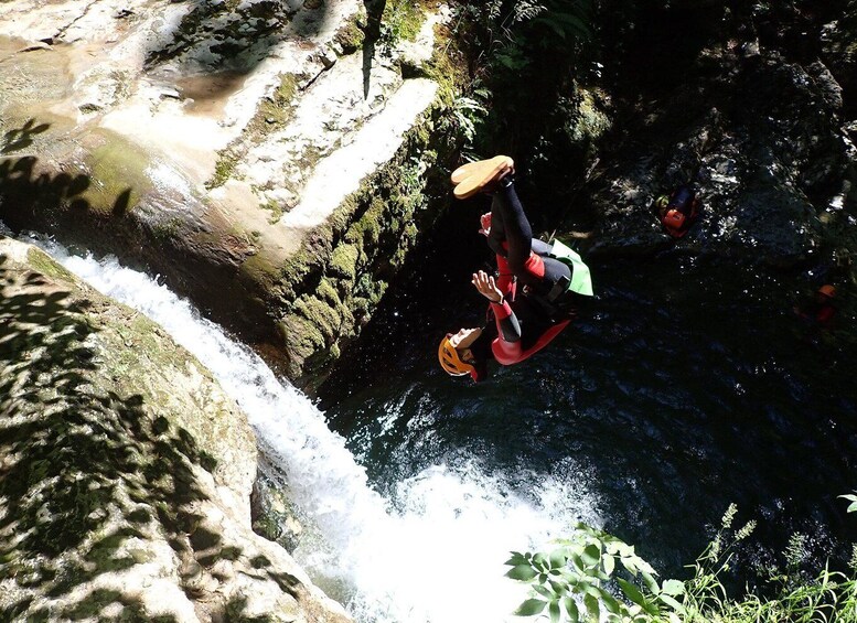 A person in a red and black wetsuit performing a backflip off a rocky waterfall. 5