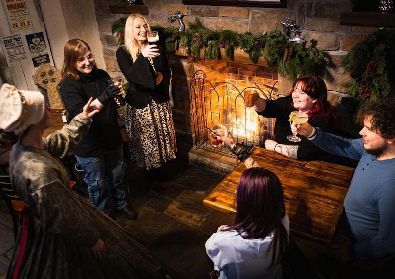 A group of people around a fireplace with Christmas decorations, holding drinks. 4
