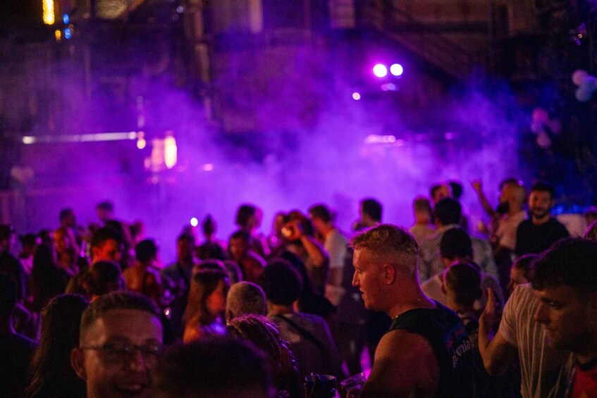 A crowded outdoor event with purple lighting and smoke effects. 3