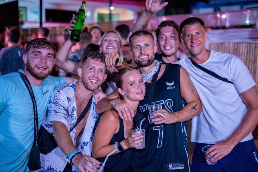 A group of people at an indoor event, some holding drinks and one holding a bottle. 1