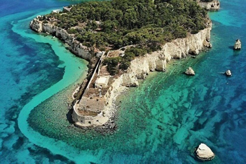 An aerial view of a coastal island with clear turquoise waters, a rocky shoreline, and a small building. 2