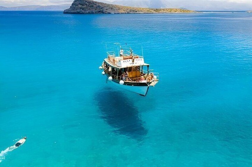 A boat floating on clear turquoise water with a rocky island in the background. 3