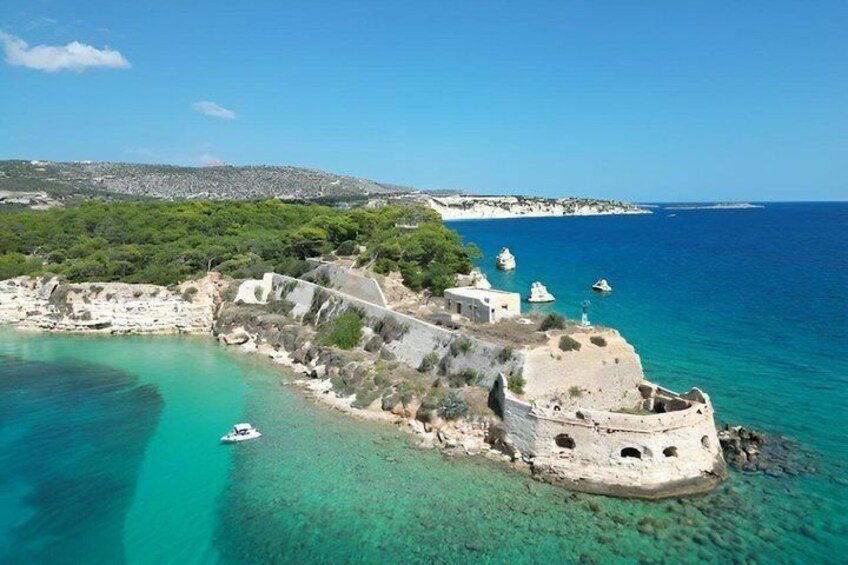 A coastal fortification with clear turquoise waters, a boat, and a distant shoreline. 1