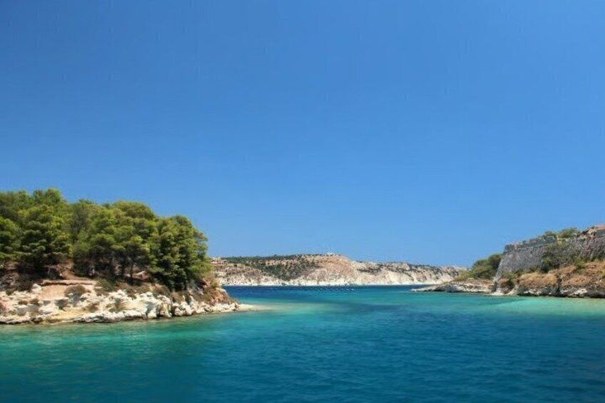 A coastal landscape with clear blue waters, rocky cliffs, and dense green trees. 5