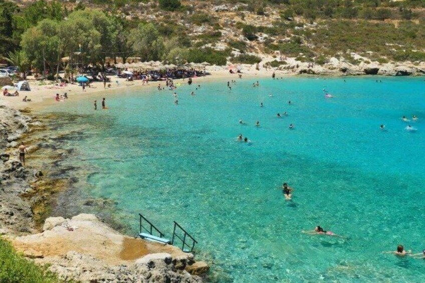A coastal beach with clear turquoise water, people swimming, and a rocky shoreline. 4