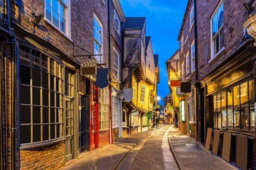 A narrow street with brick buildings, shop fronts, and a tram track. 2