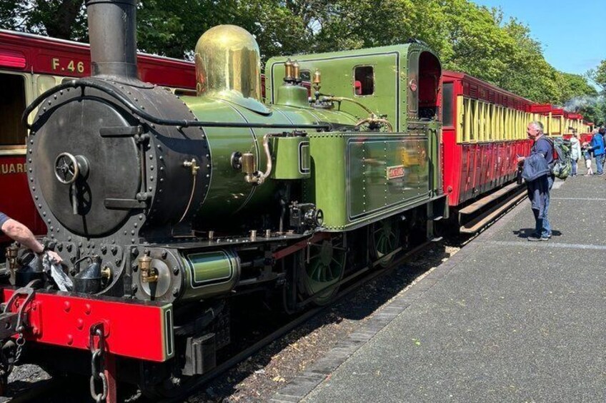 A green steam locomotive with red and yellow passenger cars at a station. 1