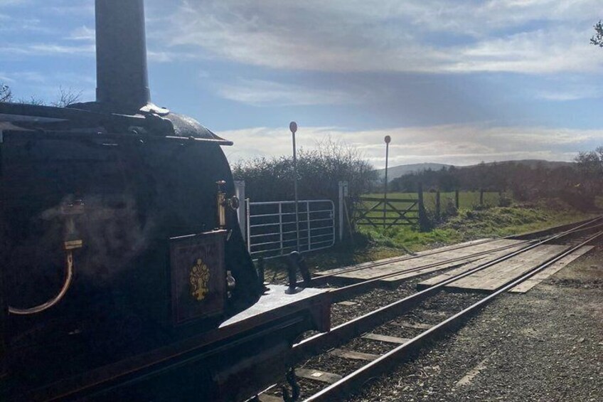 A steam locomotive at a railway crossing with tracks and a fence in the background. 5