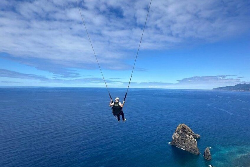 A person bungee jumping over a body of water with a clear sky and distant land. 1