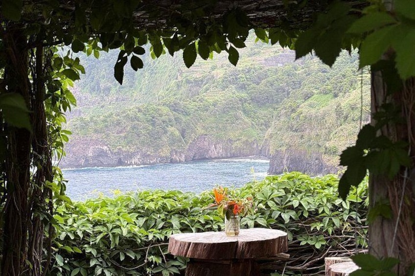 A table with a vase of flowers, surrounded by lush greenery and a view of a body of water. 3