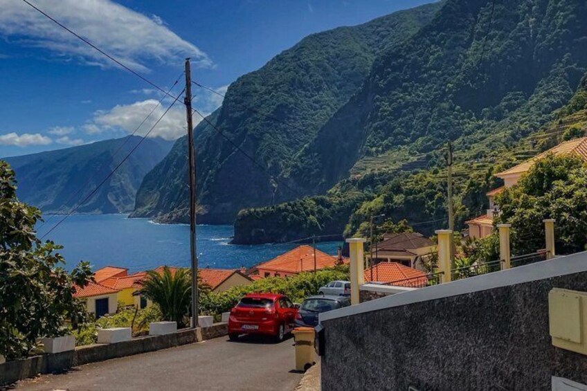 A coastal road with red-roofed houses, a red car, and a mountainous backdrop. 5