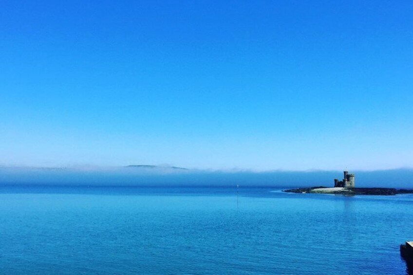 A calm sea, a small island with a tower, and a clear blue sky. 1