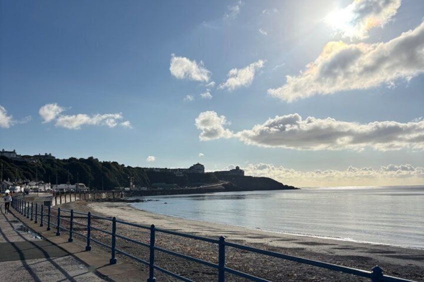 A coastal beach with a promenade, a distant hill, and a clear sky. 3