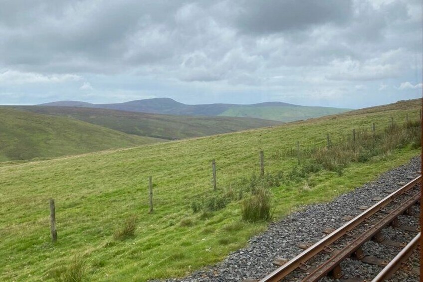 A railway track with grassy fields and distant hills under a cloudy sky. 2