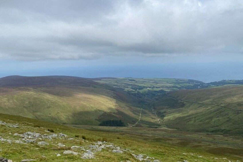 A hilly landscape with a valley and a distant view of the sea under cloudy skies. 4
