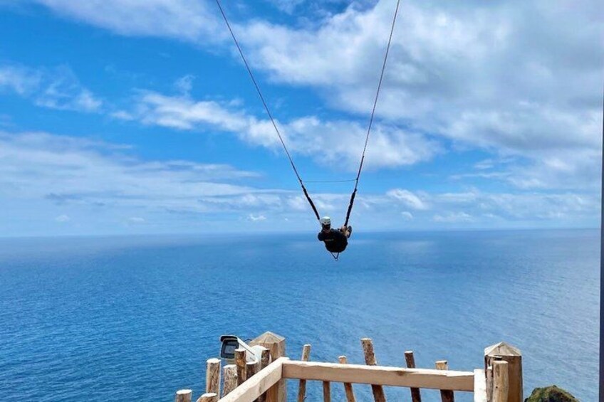 A person on a swing over a body of water with a wooden railing in the foreground. 4