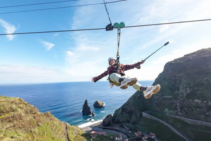 A person zip-lining over a coastal cliff with the ocean and rocky outcrops below. 1