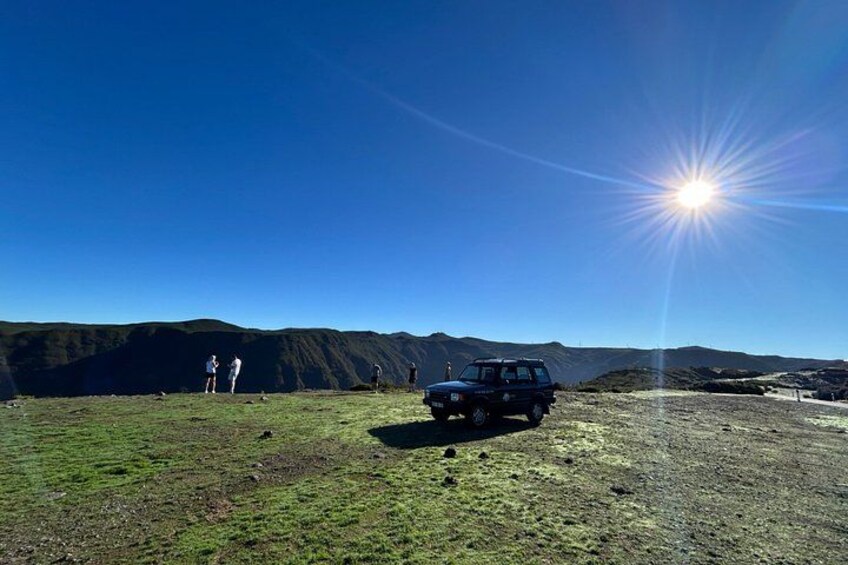 A jeep parked on a grassy field with mountains in the background and a clear blue sky. 3