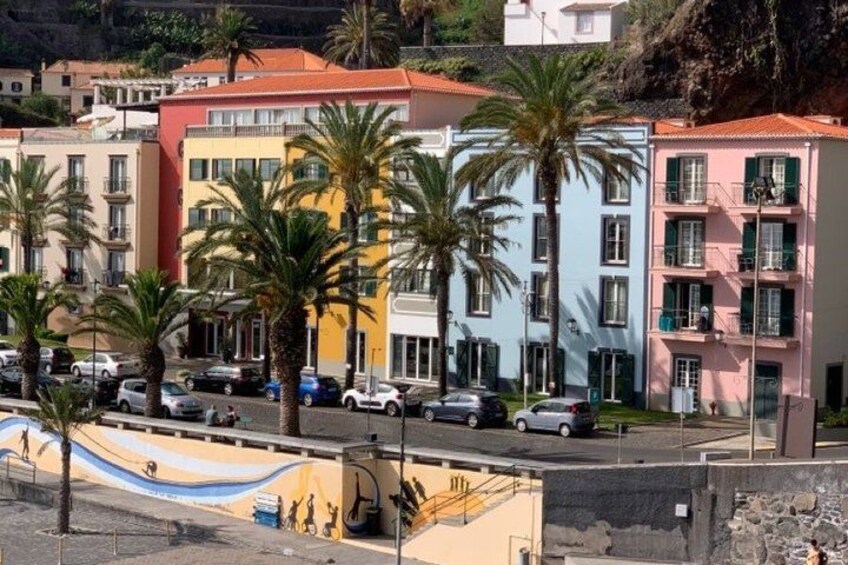 Colorful buildings, palm trees, and parked cars along a coastal street. 5
