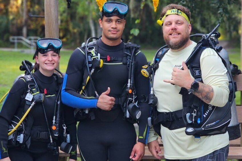 Three people wearing scuba diving gear, standing outdoors. 1