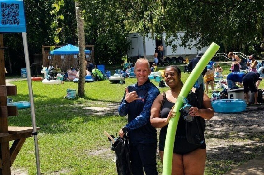 Two people holding green tubes, a blue tent, and a wooden structure in a grassy area with trees. 5