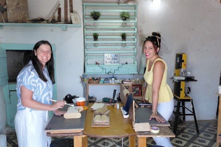 Two people in a workshop with tools and materials, a blue wall with shelves, and a sign reading 'ZOLIAS WORKSHOP.' 3
