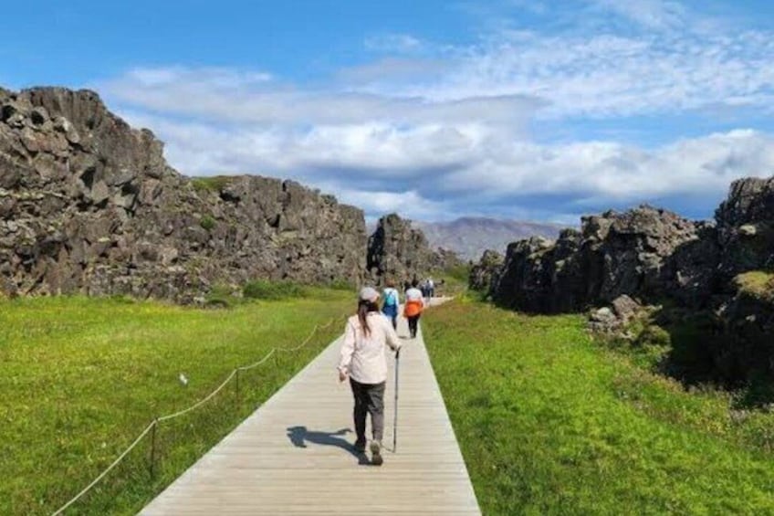 A wooden boardwalk with people walking, surrounded by rocky terrain and grassy areas. 5