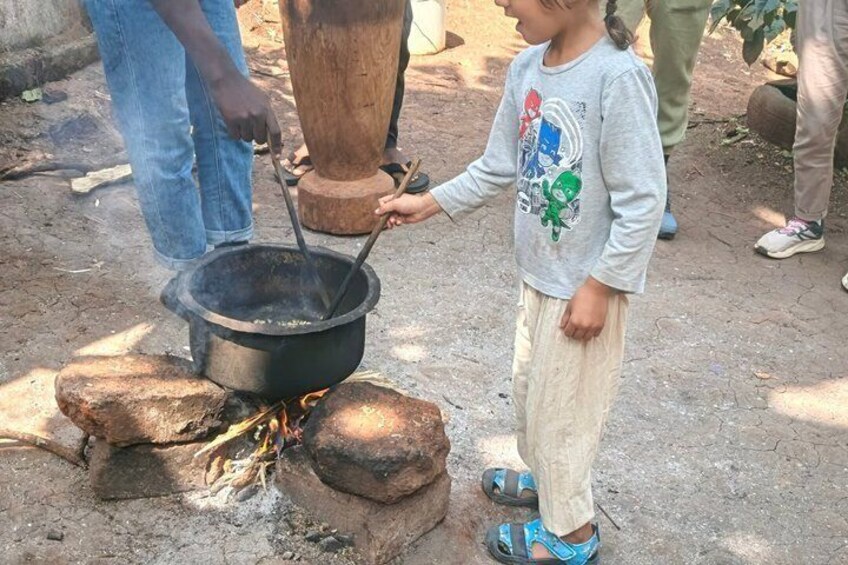 A child cooking outdoors with a pot over an open fire. 4