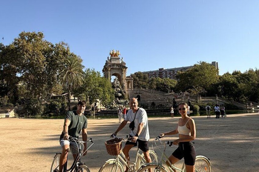Three people on bicycles in a park with a large fountain and a statue in the background. 5