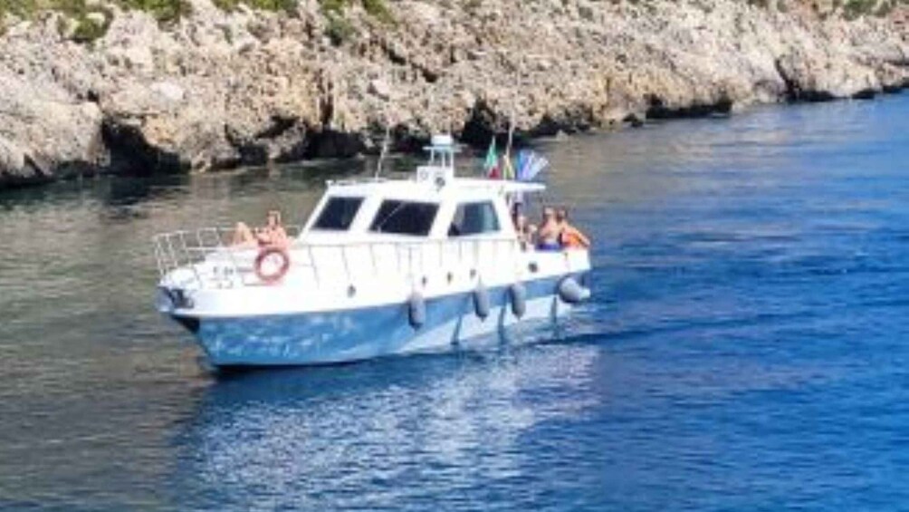 A boat with people on board, moving through a body of water with a rocky shoreline in the background. 5