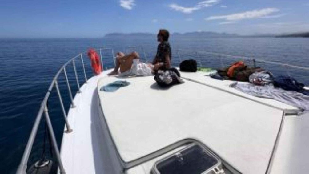A boat with a person sitting on the deck, a lifebuoy, and a bag. 2