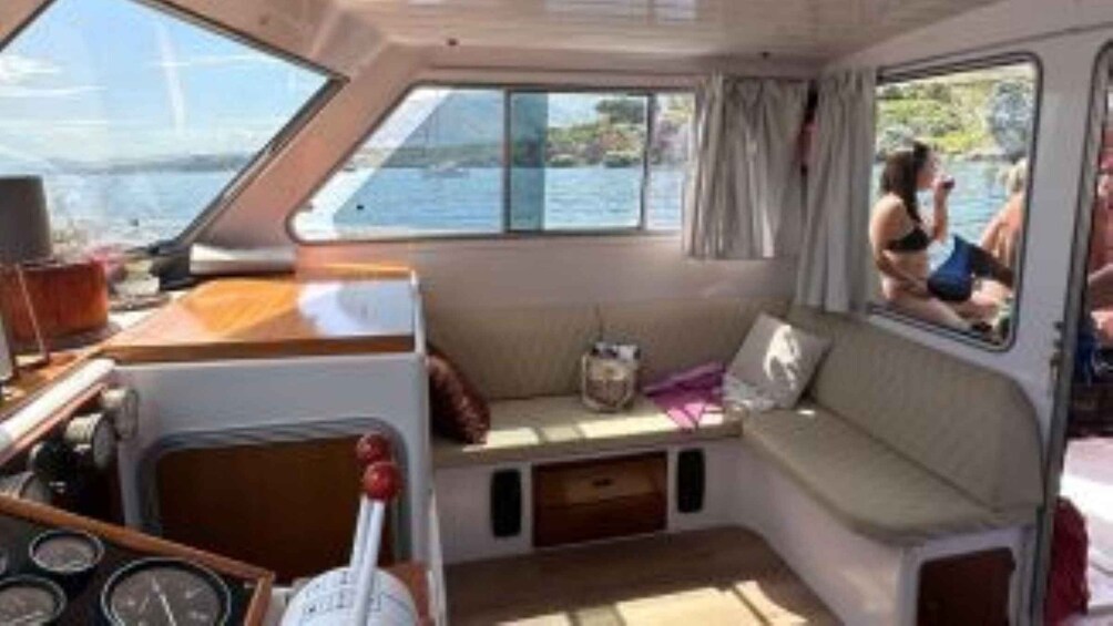A boat interior with a cushioned seating area, a steering wheel, and a window overlooking water. 4