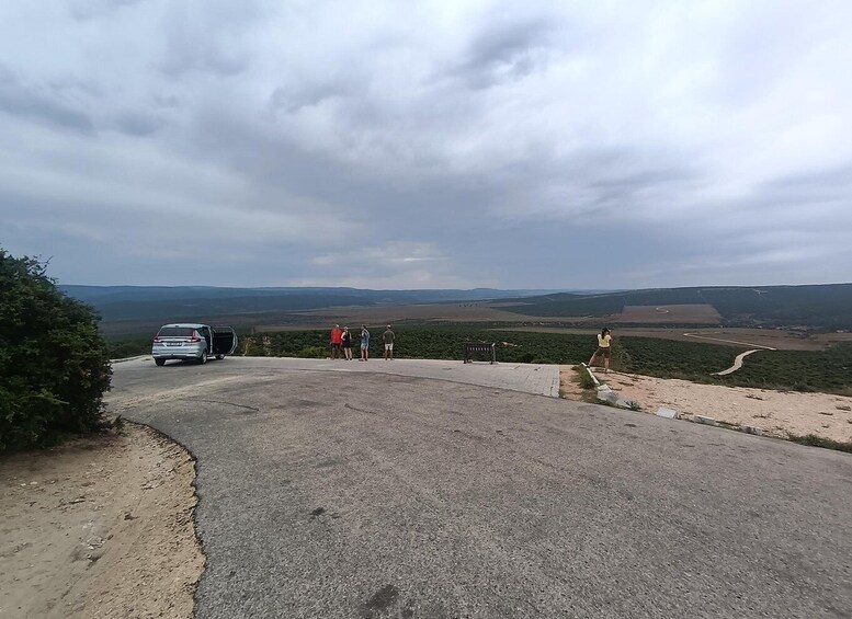 A paved road with a van, a bench, and a group of people standing on a hill overlooking a valley. 5