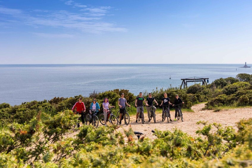 A group of people on bicycles near a coastal area with a lighthouse in the distance. 2