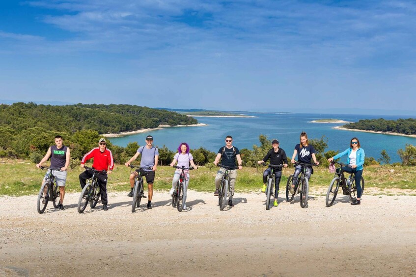 A group of people on bicycles on a dirt path with a coastal landscape in the background. 3