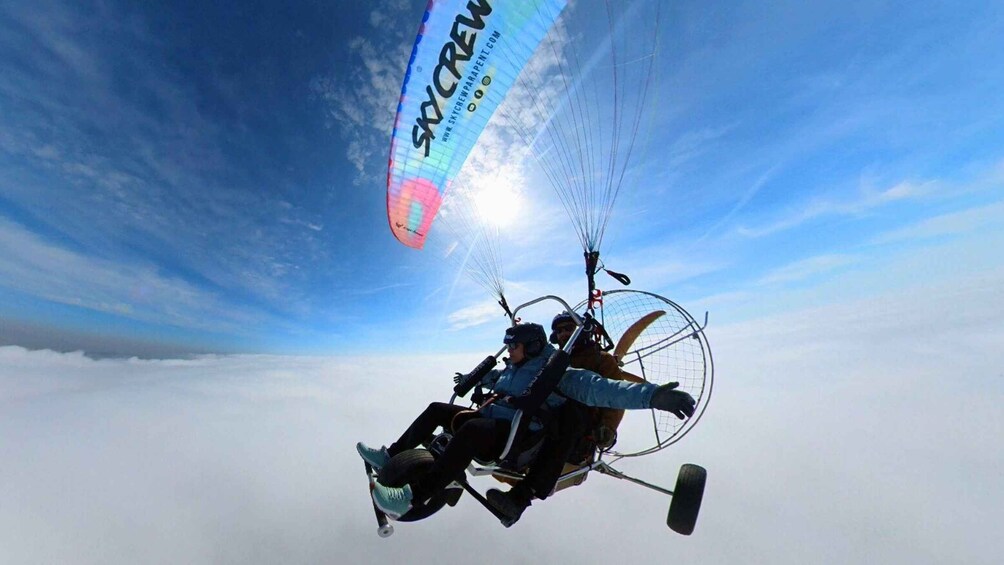 A person paragliding with a parachute labeled 'SkyCrew' against a clear sky. 2