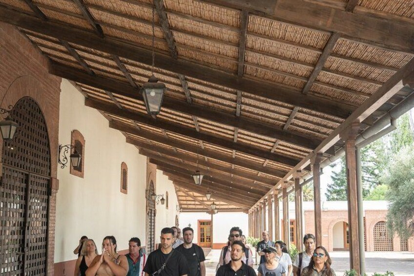 A covered walkway with wooden beams and brick walls, a group of people standing in line, and a street visible in the background. 4