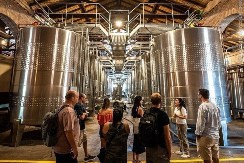 A group of people touring a facility with large cylindrical tanks. 1
