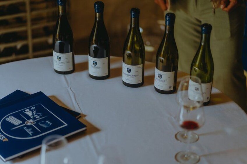 A table with wine bottles and glasses, a booklet, and a person in the background. 3