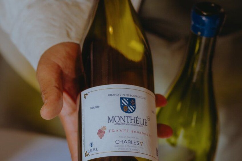 A person holding a bottle of Monthelie wine with a label that includes the text 'Grand Vin de Bourgogne' and 'Charles.' 2
