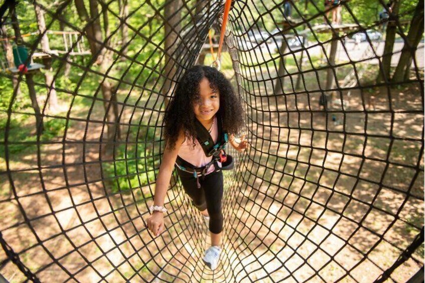 A person in a netted enclosure, possibly a playground or adventure park, with trees and a clear sky in the background. 3