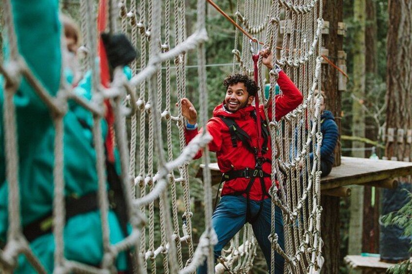 A person navigating a rope bridge in a forested area. 4