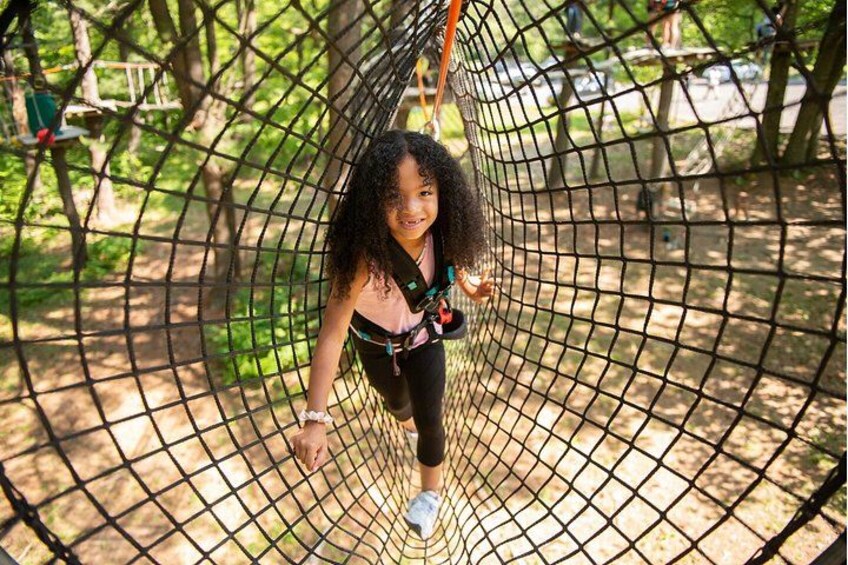 A person on a netted zip line in a wooded area. 3
