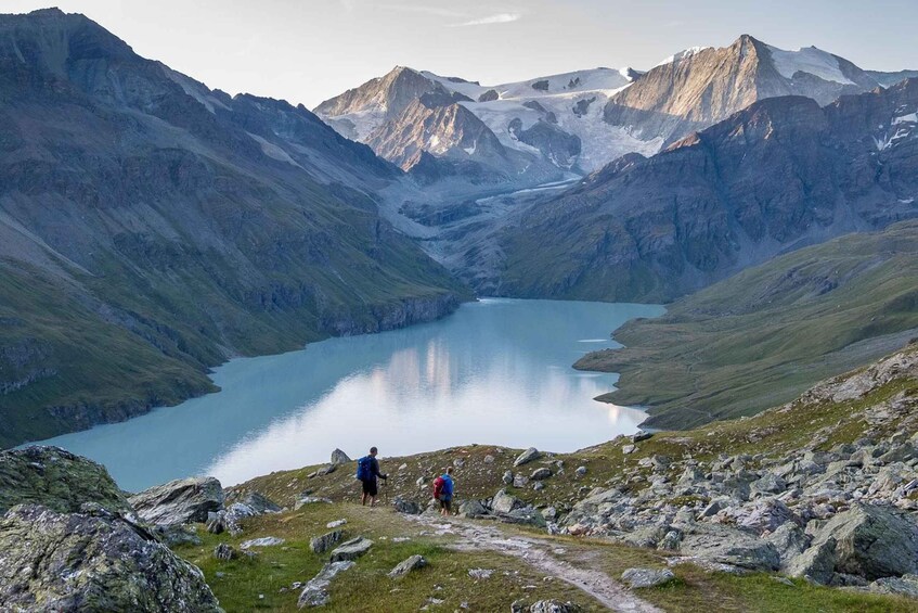 A mountainous landscape with a lake and two hikers. 1