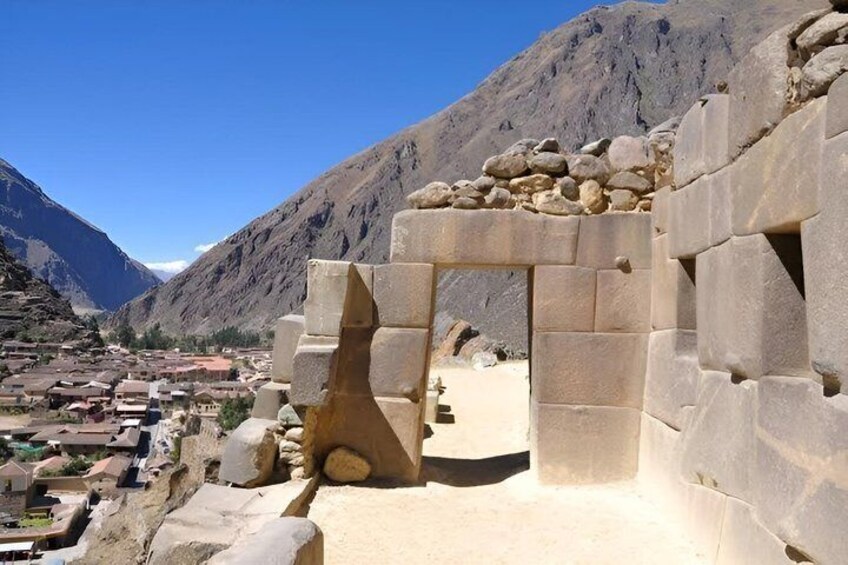 A stone structure with a large archway, a mountainous backdrop, and a village in the distance. 4
