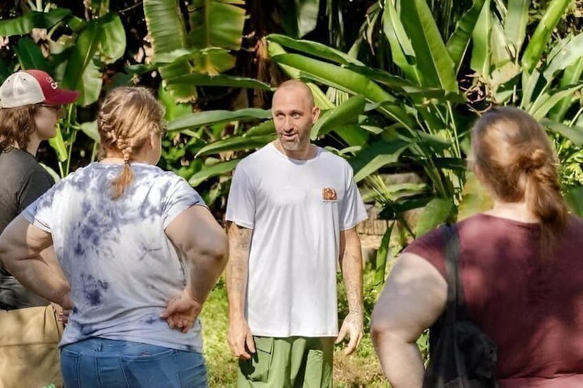 A group of people standing outdoors with large green leaves in the background. 1